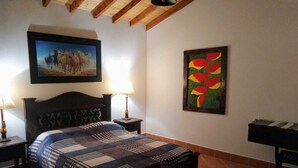Un dormitorio con una cama, dos mesitas de noche, una lámpara, un cuadro de caballos y un cuadro de flores.
