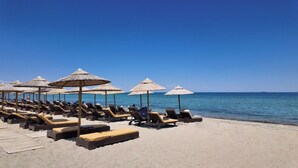 Une plage avec des chaises longues et des parasols en chaume.