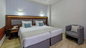 A hotel room with a large bed, two bedside tables, a chair, and a wall-mounted light fixture. - Eona Beach Resort (Thermaikos)