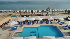 A pool area with blue lounge chairs and umbrellas, a clear view of the sea, and a building with a tiled roof. - Eona Beach Resort (Thermaikos)