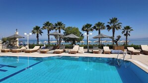 Une piscine avec des chaises longues et des parasols, des palmiers, et une vue sur la mer.