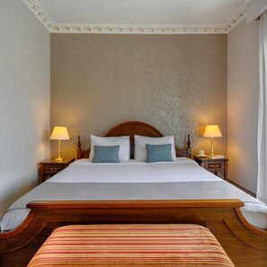 A hotel room with a large bed, two bedside tables with lamps, a wooden headboard, and a striped bench. - Eona Beach Resort (Thermaikos)