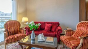 A hotel room with a red sofa, striped armchairs, a glass coffee table, a vase with flowers, and a chandelier. - Eona Beach Resort (Thermaikos)