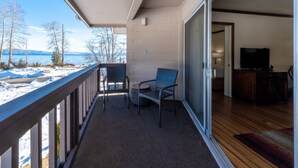 Een balkon met uitzicht op een meer en bergen, een stoel, en een televisie in de aangrenzende kamer.