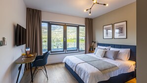 Un dormitorio moderno con una cama grande, un escritorio y una silla. Hay dos cuadros enmarcados en la pared y una ventana con vistas al exterior.
