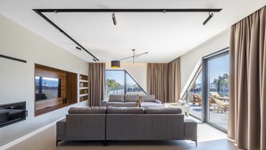 Una sala de estar moderna con un sofá seccional gris grande, un televisor de pantalla plana montado en la pared y un ventanal con vistas al exterior.