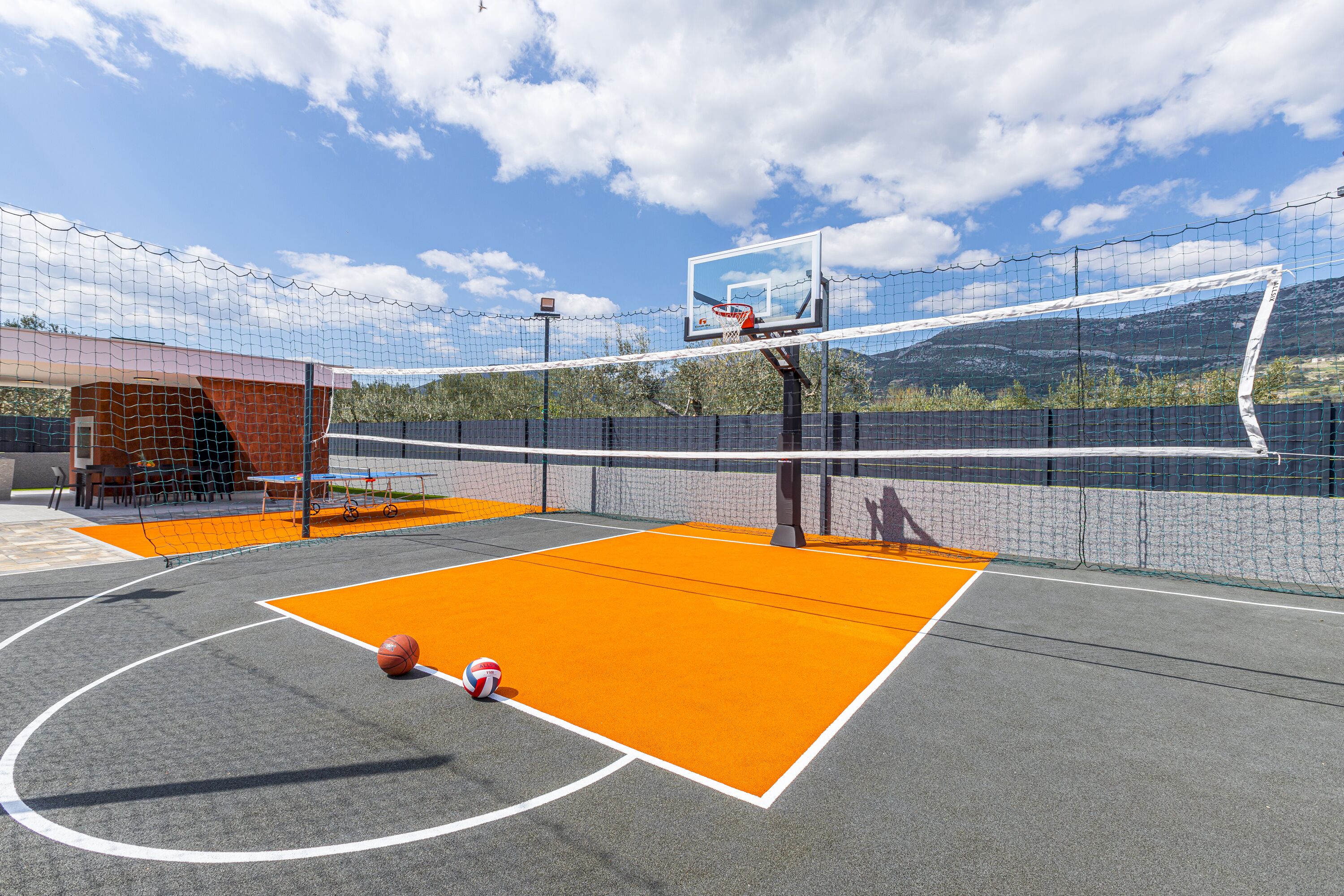 An outdoor basketball court with a net, a basketball, and a volleyball.