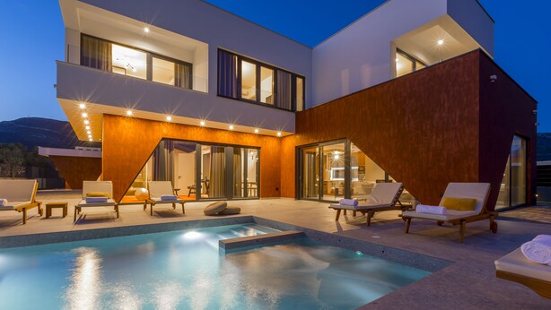Una casa moderna de dos pisos con piscina, mobiliario exterior y una entrada bien iluminada.