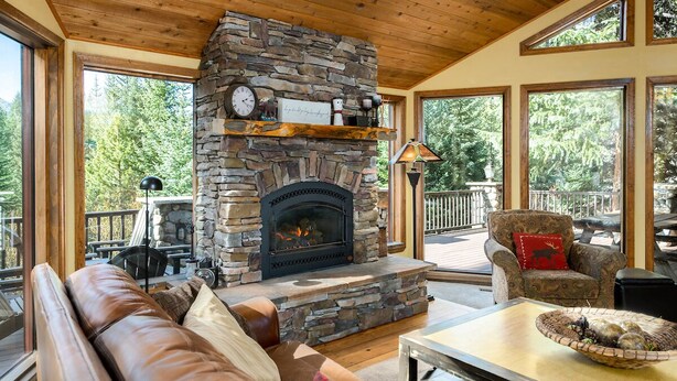 A stone fireplace with a clock above it, a leather sofa, and a dining table with a decorative bowl.