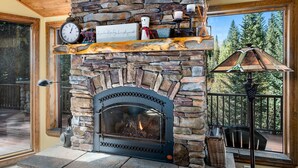 A stone fireplace with a clock above it, a shelf with decorative items, and a view of the outdoors through a large window.