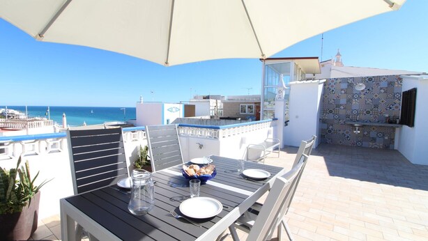 An outdoor dining area with a table set for two, a large umbrella, and a view of the sea. - House of the Sun - VoudeFerias.pt (Albufeira)
