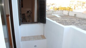 A small balcony with a white wall, a window with black shutters, and a view of a cityscape. - House of the Sun - VoudeFerias.pt (Albufeira)