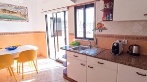 A kitchen with a sink, countertop, and cabinets. There is a dining table with chairs and a window with a view. - House of the Sun - VoudeFerias.pt (Albufeira)