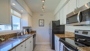 A modern kitchen with white cabinets, granite countertops, stainless steel appliances, and a window providing natural light. - SCOTTSDALE CONDO/OLDTOWN ACROSS STREET FROM FASHION SQUARE MALL...NEW REMODEL (Scottsdale)