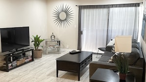 A modern living room with a flat-screen TV, dark wooden coffee tables, a sofa, and a large window with curtains. - SCOTTSDALE CONDO/OLDTOWN ACROSS STREET FROM FASHION SQUARE MALL...NEW REMODEL (Scottsdale)