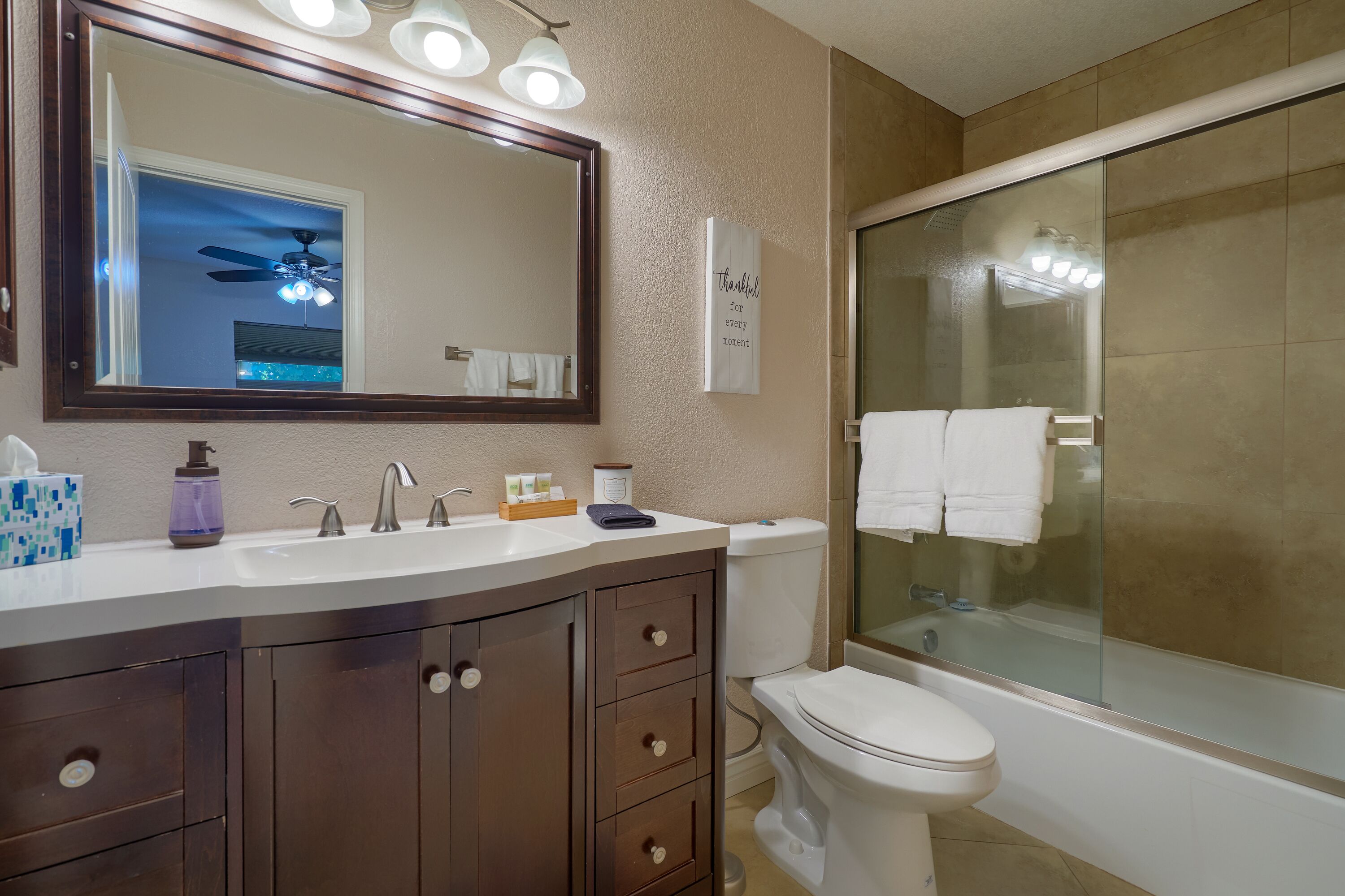 A bathroom with a large mirror, a vanity with a sink, a toilet, and a shower area.