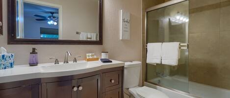 A bathroom with a large mirror, a vanity with a sink, a toilet, and a shower area.