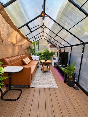 A greenhouse with a leather sofa, a small table, and potted plants.