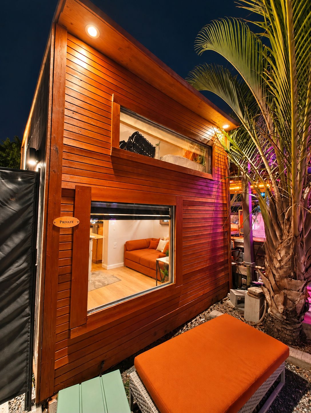 Un bâtiment moderne avec une façade en bois, une entrée dotée d’une porte en verre et un canapé orange à l’intérieur.