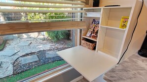 A modern kitchen with a built-in desk, a large window with blinds, and a flat-screen TV mounted on the wall. - Tiny House , Big Vibes Illuminated Backyard Escape (St. Petersburg)