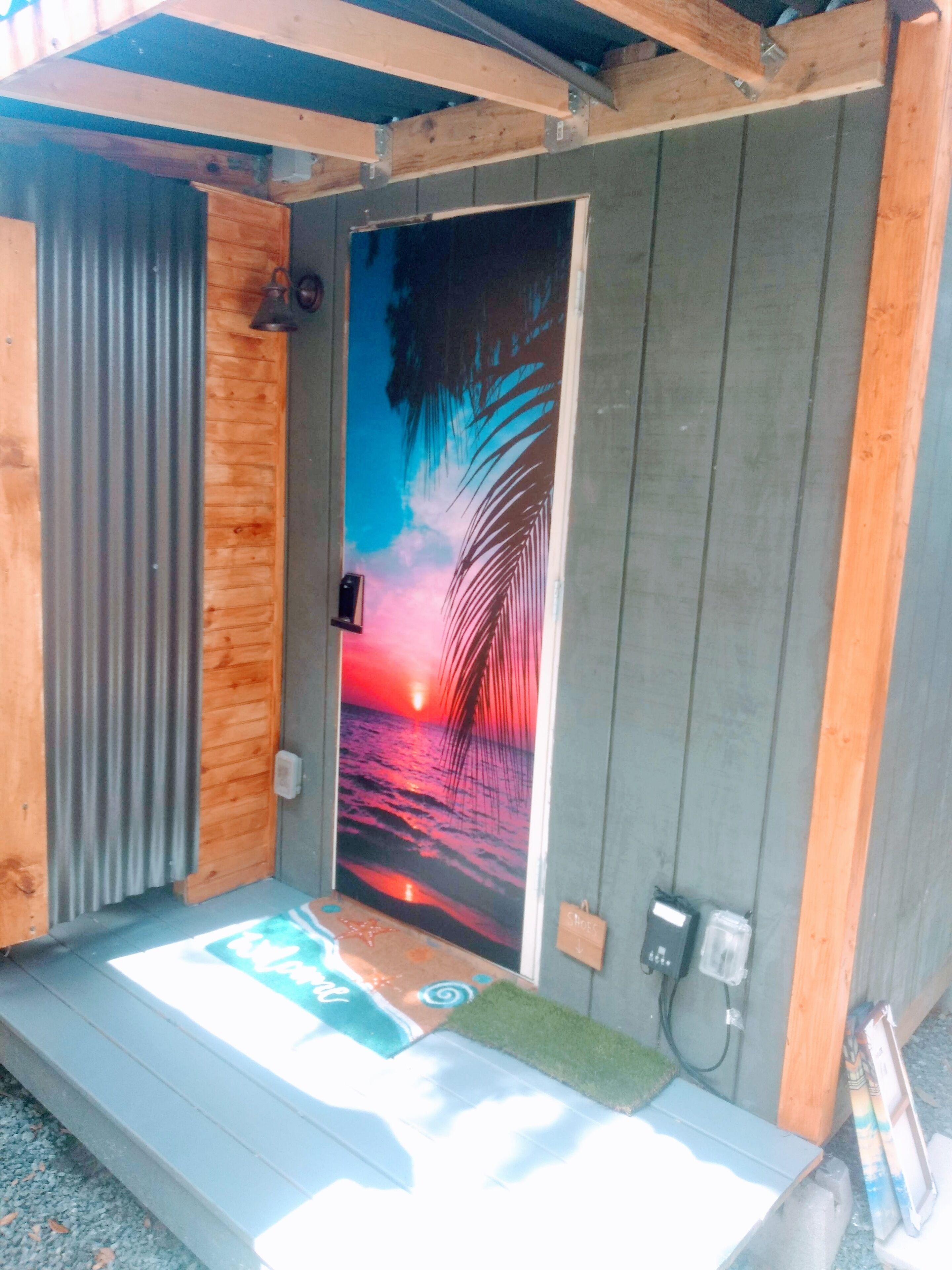 A wooden structure with a door featuring a sunset and palm tree mural.