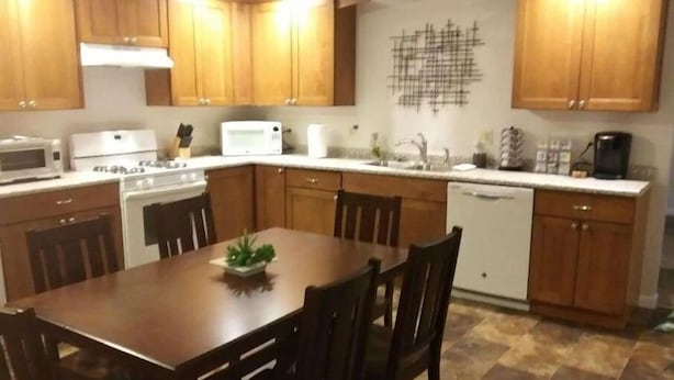 A kitchen with wooden cabinets, a stove, microwave, and a dining table with chairs. - Lyle &Taylor Present -Slice of Home on the Road (Bourbonnais)