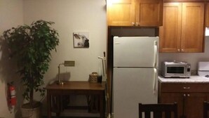 A compact kitchen with wooden cabinets, a white refrigerator, a microwave, a dining table, and a potted plant. - Lyle &Taylor Present -Slice of Home on the Road (Bourbonnais)