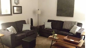 A living room with two dark sofas, a wooden coffee table, and a floor lamp. - Lyle &Taylor Present -Slice of Home on the Road (Bourbonnais)
