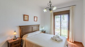 Een hotelkamer met een bed, nachtkastje met lamp, raam met gordijnen en uitzicht op de omgeving.