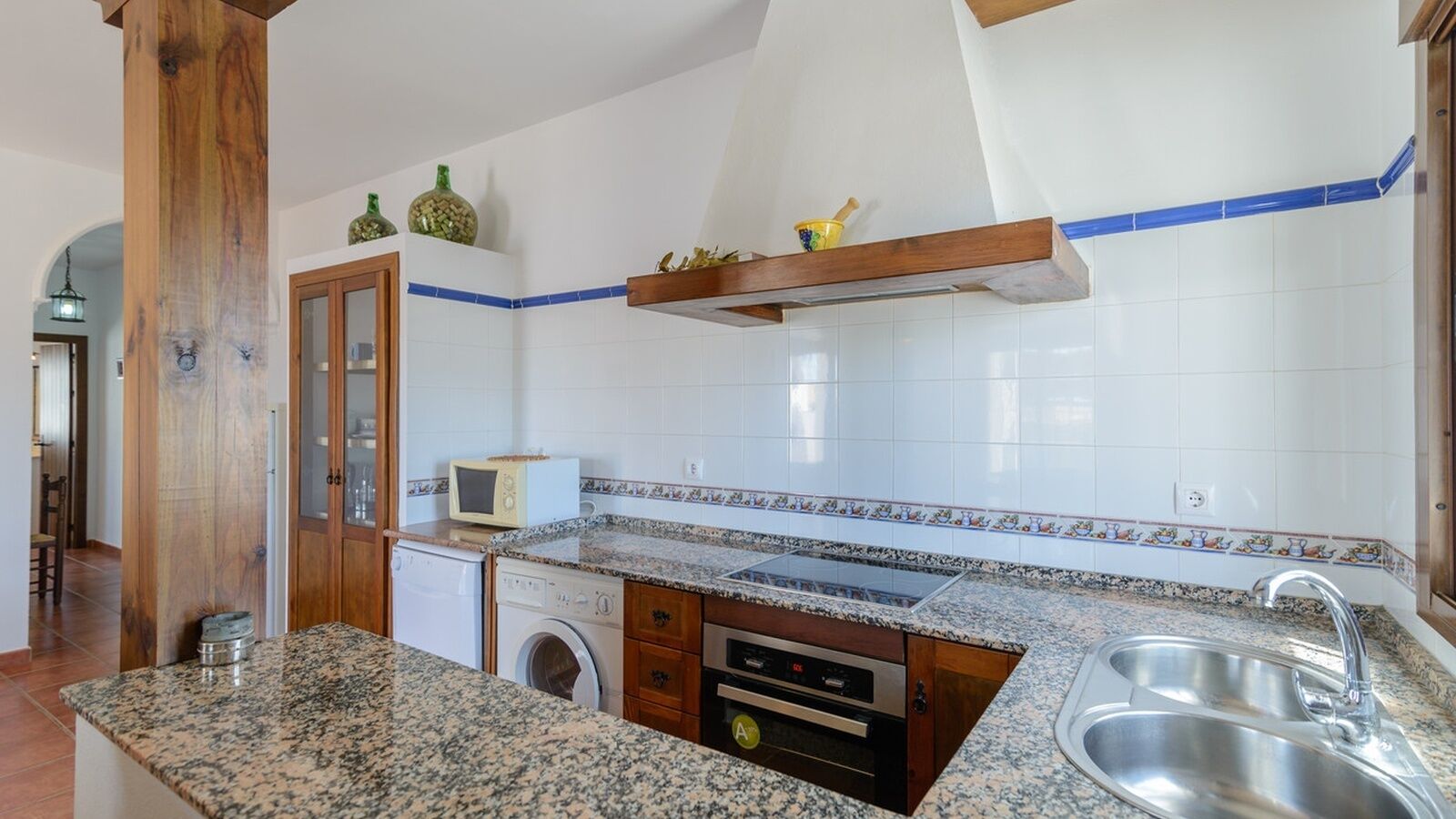 Een keuken met granieten aanrecht, een ingebouwde oven, een magnetron, een spoelbak en een wasmachine.