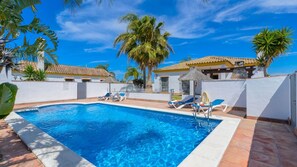 A swimming pool with lounge chairs, palm trees, and a building with a tiled roof. - Casas Villanueva - Casa 3 Conil de la Frontera by Ruralidays (Cádiz)