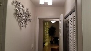 Un pasillo con una lámpara en el techo, un adorno en la pared y una puerta que da a otra habitación.