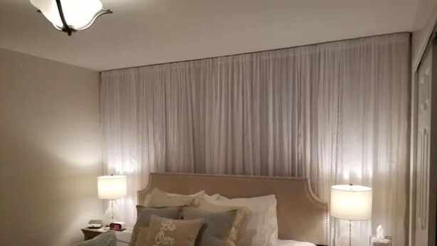 Una cama bien hecha con cabecera, dos lámparas de noche y una mesita de noche con lámpara y caja de pañuelos.
