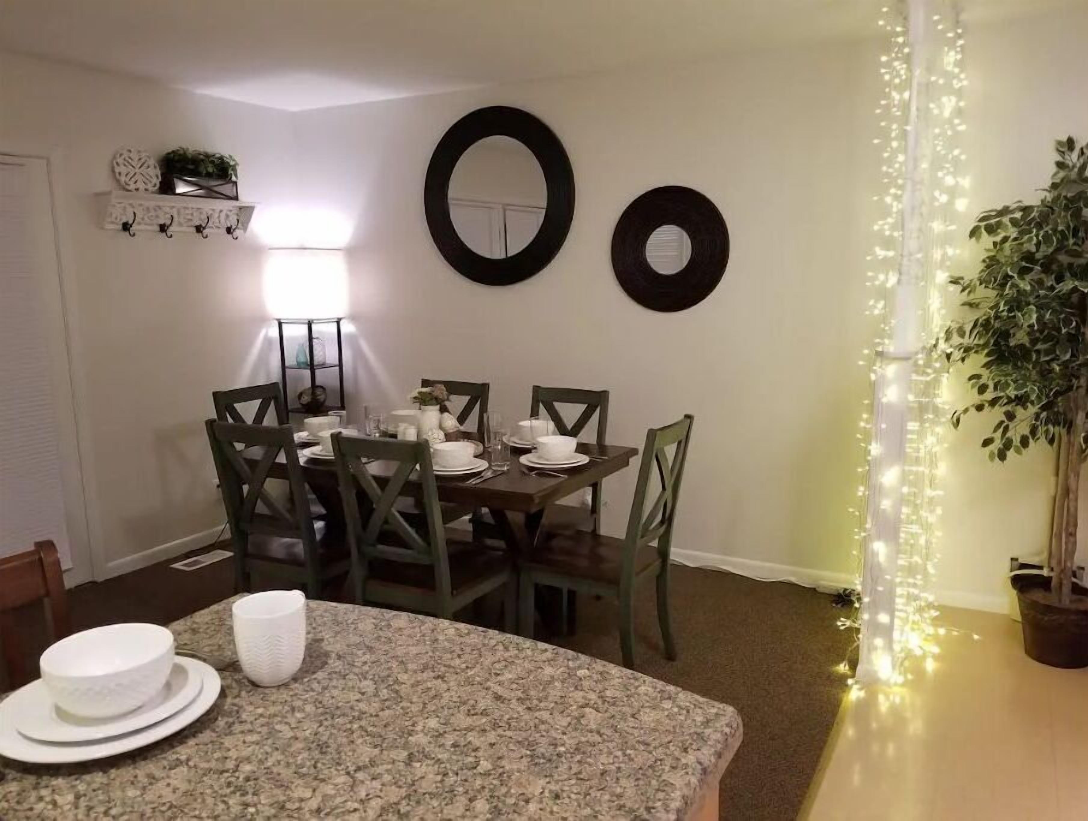 Un comedor con una mesa redonda dispuesta para cuatro personas, rodeada de sillas. Encima de la mesa hay platos decorativos colgados en la pared.