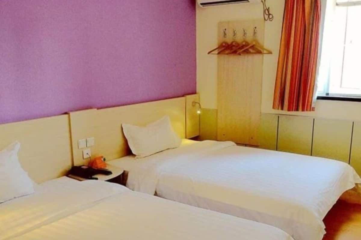 A hotel room with two beds, a nightstand, a lamp, and a window with curtains.