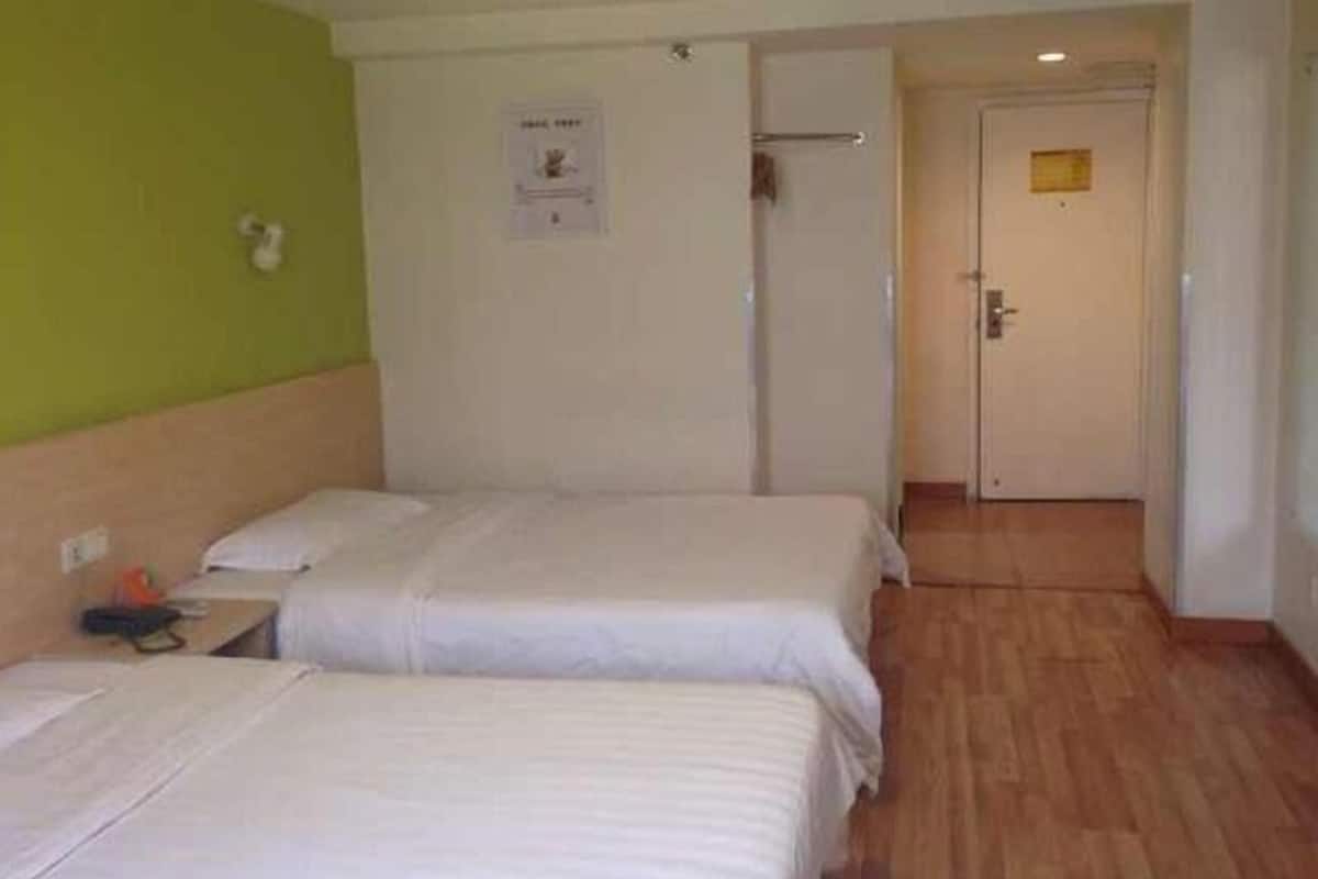 A hotel room with two beds, a wooden floor, a green wall, and a door leading to another room.