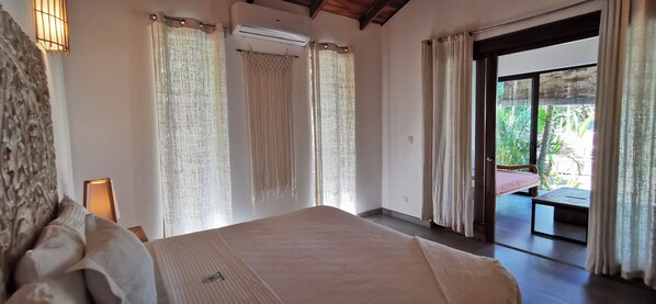 A bedroom with a bed, curtains, an air conditioning unit, and a view of the outdoors.