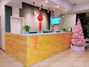 A reception desk with a number 7 sign, a digital screen, a red hanging ornament, and a pink Christmas tree. - 7 Days Premium (Guangzhou Zengcheng Xintang Light Rail Metro Station) (Guangzhou)