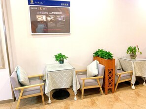 A hotel lobby with three tables, each with a plant and a chair. A large screen displays information. - 7 Days Premium (Guangzhou Zengcheng Xintang Light Rail Metro Station) (Guangzhou)
