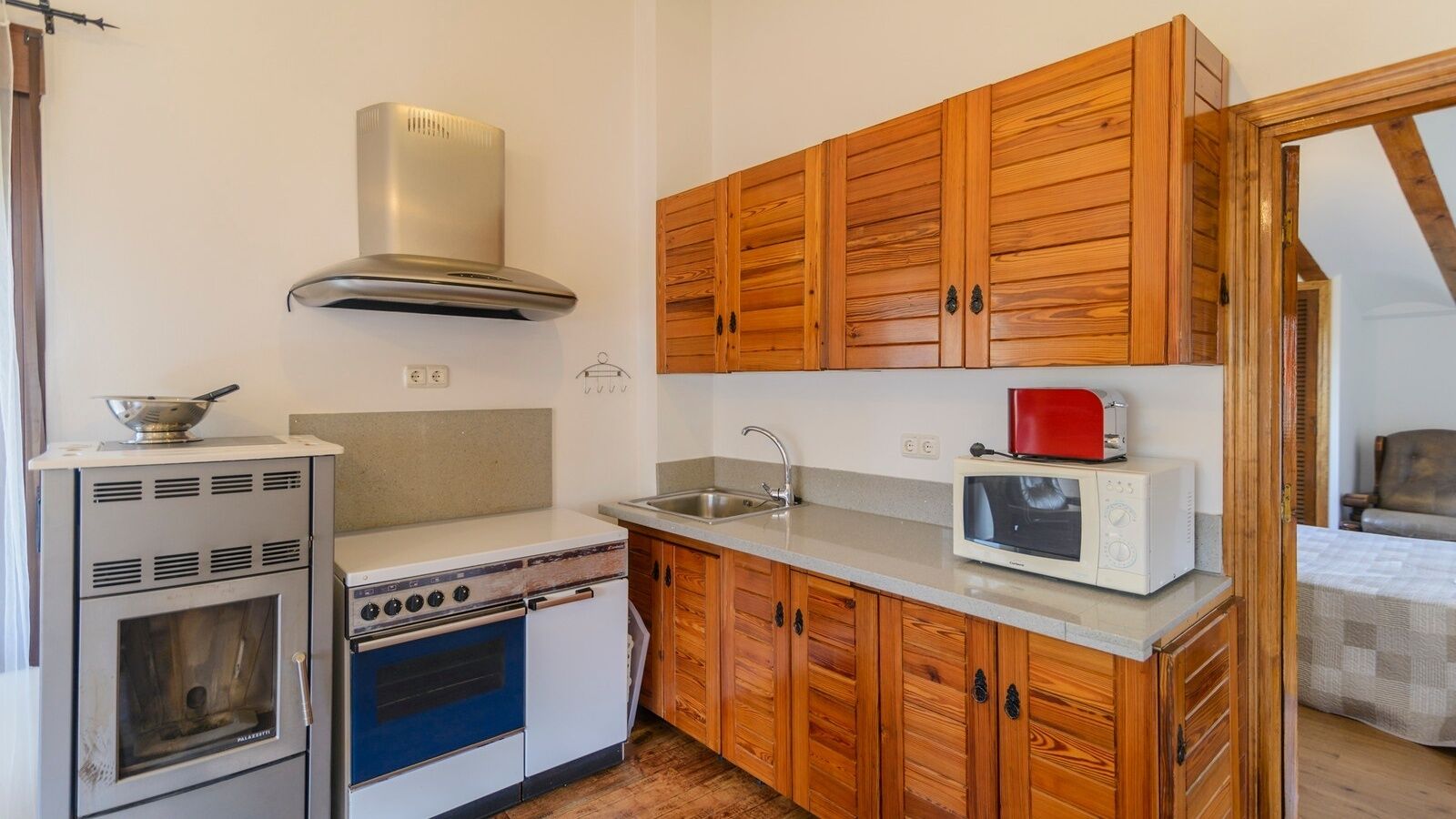 A compact kitchen with wooden cabinets, a stove, a microwave, and a sink.