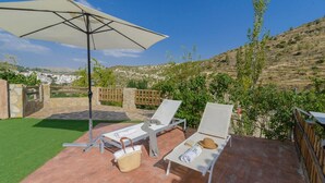 A patio with two sun loungers, a large umbrella, and a stone wall. - Cortijo la Era Castril by Ruralidays (Granada)