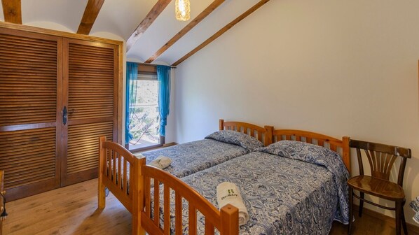A bedroom with two wooden beds, a wooden chair, and a window with blue curtains. - Cortijo la Era Castril by Ruralidays (Granada)