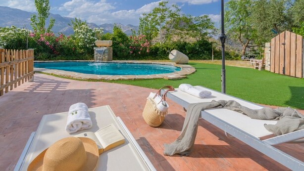 A poolside area with lounge chairs, a book, and a straw hat. - Cortijo la Era Castril by Ruralidays (Granada)