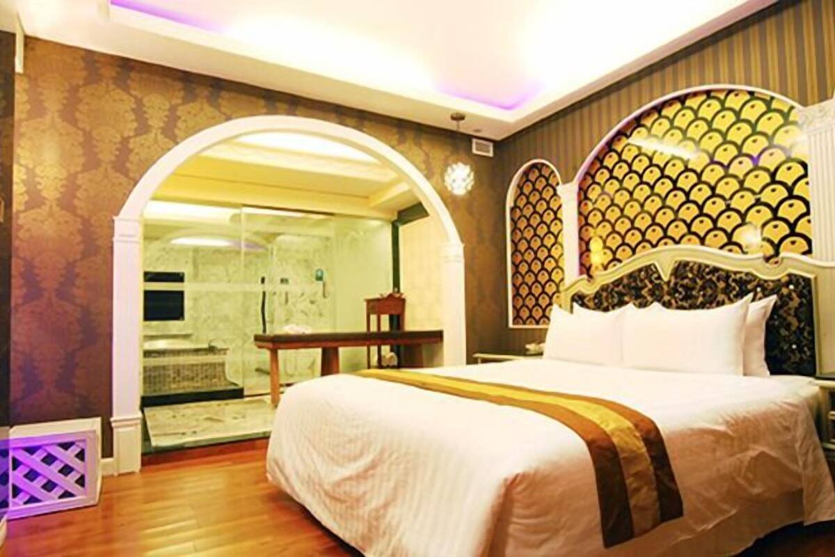A hotel room with a large bed, a desk, and a bathroom visible through an arched doorway.