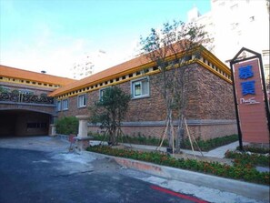 A building with a stone facade and a yellow roof. There is a sign with Chinese characters and a small garden area with plants and flowers. - Mucha Motel (Kaohsiung)