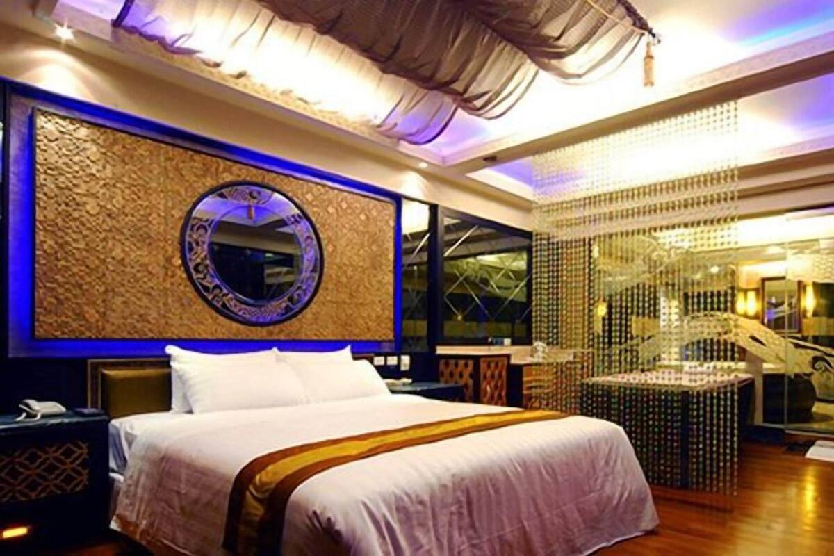 A modern hotel room with a large bed, a round mirror, and a decorative wall.