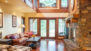 A spacious living room with a stone fireplace, leather sofa, and a view of the outdoors through large glass doors. - Golf View, Game Room, Suncadia Pool Access (Cle Elum)