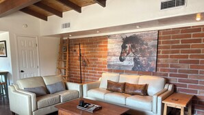 A living room with a brick wall, two leather sofas, a wooden coffee table, and a ladder against the wall. - Quiet 3 acre Ranch Home with incredible mountain views!! (Tucson)