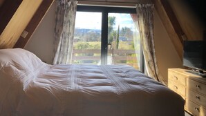 Een slaapkamer met een groot bed, een dressoir en een raam met gordijnen.