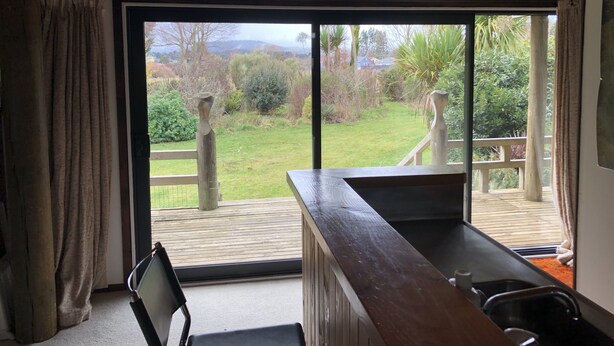 Een kamer met een grote schuifglazen deur die uitkomt op een terras, een houten tafel en een stoel.